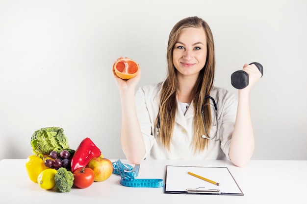 Female dietician holding grapefruit and dumbbell in clinic Free Photo