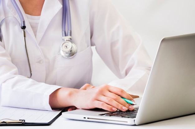 A female doctor with stethoscope around her neck using laptop on desk Free Photo