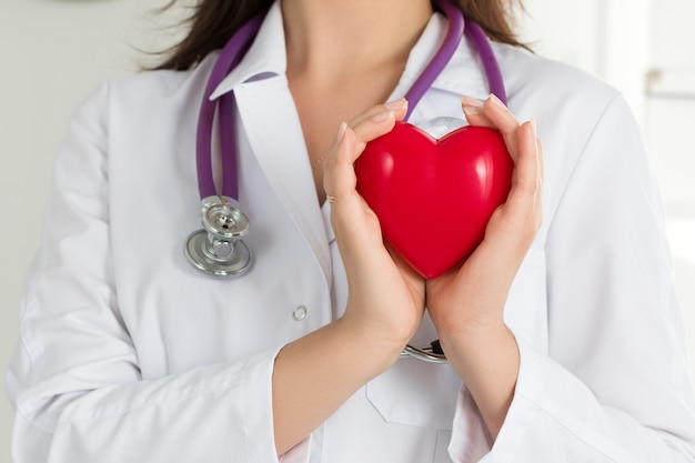  Female doctors's hands holding red heart in front of her chest. doctor's hand closeup. medical help