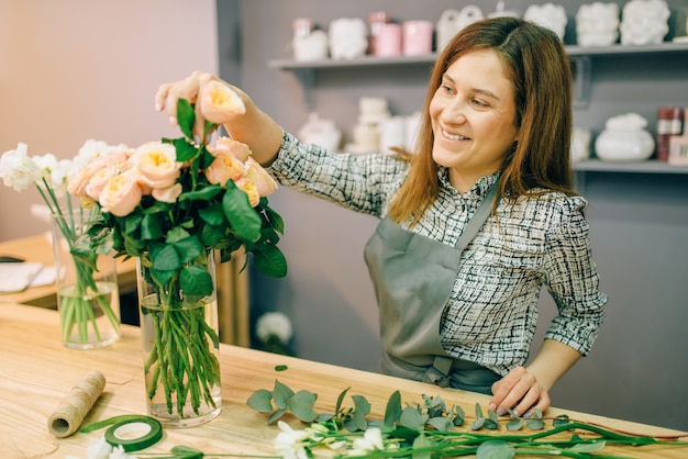 Premium Photo | Female florist in apron puts fresh roses in a vase in ...