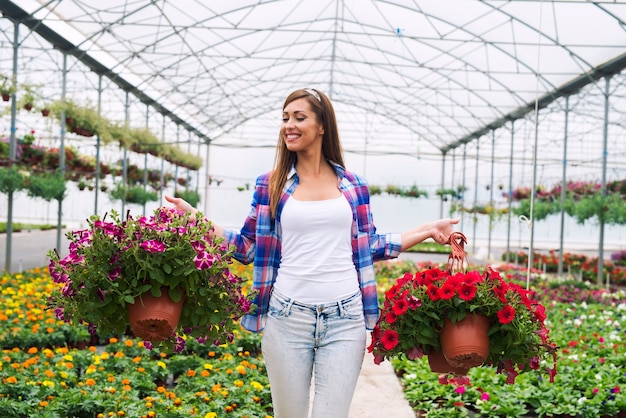 温室で鉢植えの花の植物を運んで販売のためにそれらを配置する女性の花屋 無料の写真