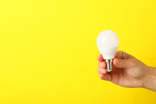 Premium Photo | Female hand holds energy saving bulb on yellow background.