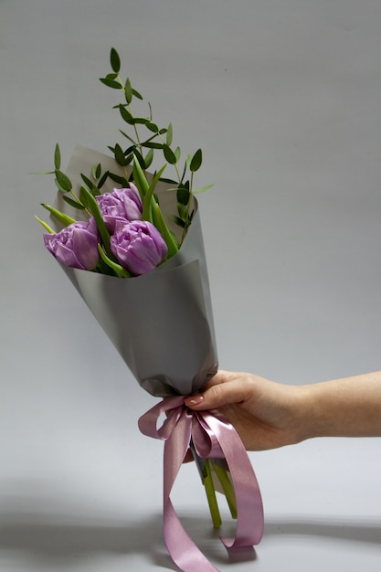 紫のチューリップとラスクス セレクティブフォーカスのミニマルな春の花束を保持している女性の手 プレミアム写真