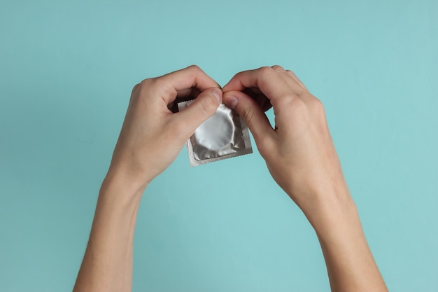 Premium Photo | Female hands open a condom on blue paper