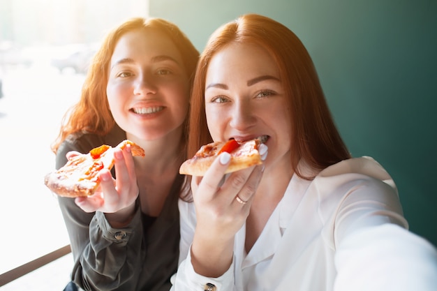 女性モデルは カフェで電話で自撮りをします 笑顔でピザを食べる若い女性 プレミアム写真