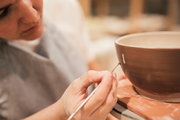 Female potter's hand drawing design on the outer surface of bowl with tool Free Photo