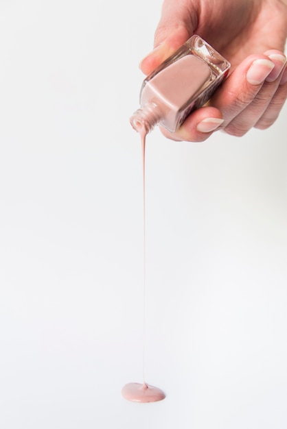 女性の手が白い背景の上のマニキュア液をこぼす プレミアム写真