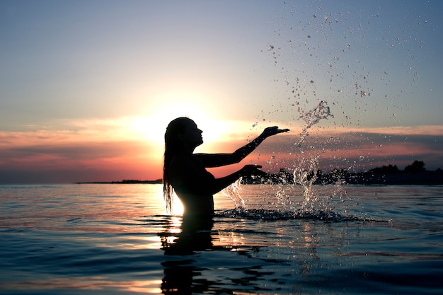 海に沈む夕日の女性のシルエットは 水のしぶきを作る プレミアム写真