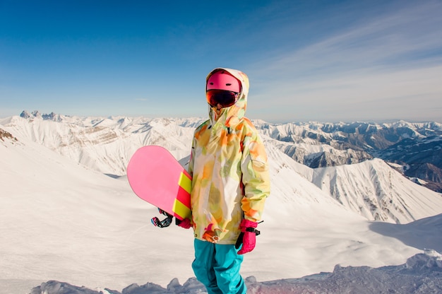 ジョージア州 グダウリの山の頂上に立っている明るいスポーツウェアの女性スノーボーダー プレミアム写真