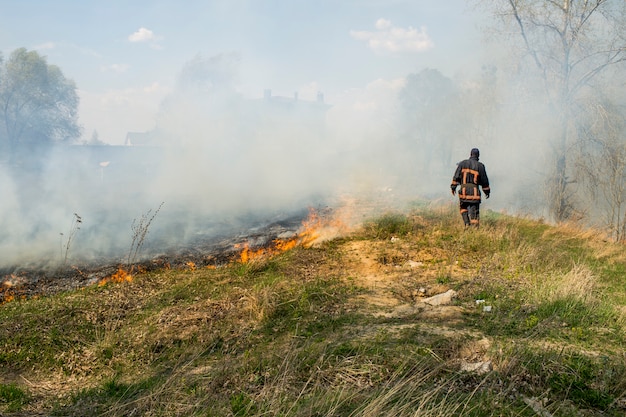 火の背景に消防士 春の草や小枝で燃える山火事 プレミアム写真