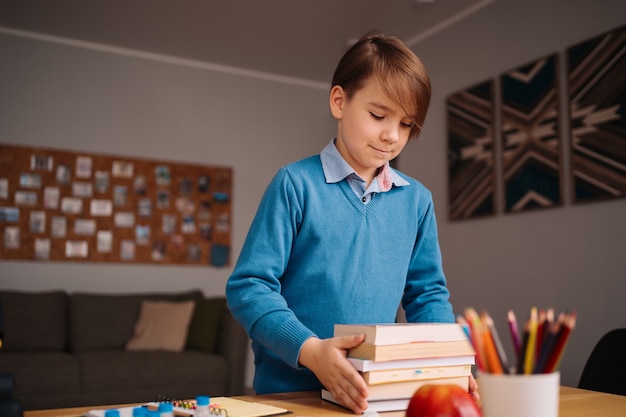 家で勉強し たくさんの本を持って オンラインレッスンの準備をしている一年生の男の子 無料の写真