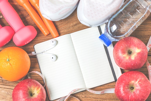 Fitness, healthy and active lifestyles concept, bottle of water, dumbbells, sport shoes, smartphone with headphone and apples on wood background. copy space for text. top view Free Photo