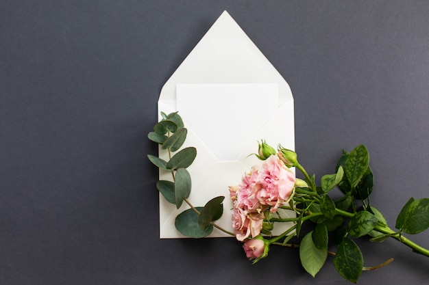 Flat lay composition with a white envelope, blank card and a peony rose flower on a grey background. mockup for wedding or valentine's day. top view. Premium Photo