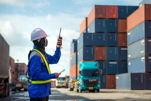 Foreman using and talking walkie talkie to control loading containers box to truck at container depot station for logistic import export scene Premium Photo