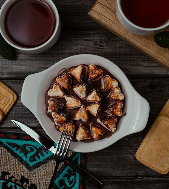 Fork ready to pick one of a finely cooked heart shape cookies from a white platter Free Photo