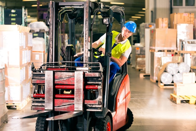 Forklift driver in protective vest driving forklift at warehouse of freight forwarding company Premium Photo