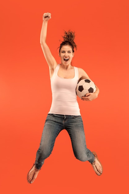 勝利に向けて 赤い背景のスタジオでジャンプしてボールを蹴るサッカーサッカー選手としての若い女性 サッカーファンと世界選手権のコンセプト 人間の感情の概念 無料の写真