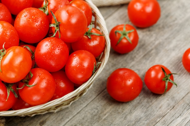 Fresh red tomatoes in a wicker basket on an old wooden table. ripe and juicy cherry tomatoes with drops of moisture, gray wooden table, around a cloth of burlap. in a rustic style. Premium Photo