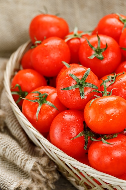 Fresh red tomatoes in a wicker basket on an old wooden table. ripe and juicy cherry tomatoes with drops of moisture, gray wooden table, around a cloth of burlap. in a rustic style. Premium Photo