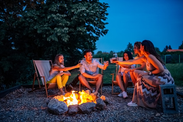 Premium Photo | Friends toasting while sitting around fire pit.