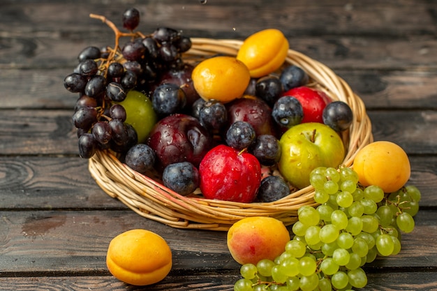 茶色の素朴な机の上の果物のアプリコットプラムなどの果物のまろやかで酸っぱい果物が入った正面バスケット 無料の写真