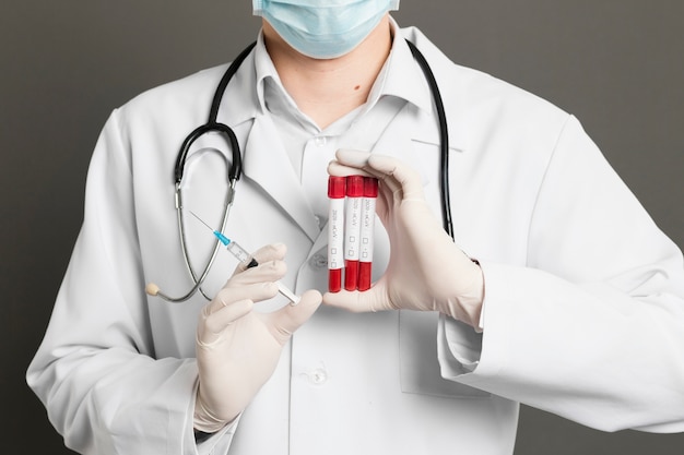 Front view of doctor with medical mask holding syringe and vacutainers Free Photo