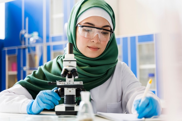 Front view of female scientist with hijab and microscope | Free Photo