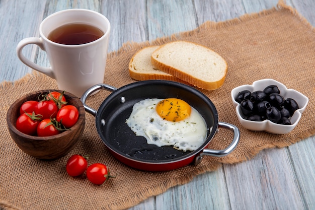 Download Free Photo | Front view of fried egg in pan with bowl of tomato and tea with bread slices and ...