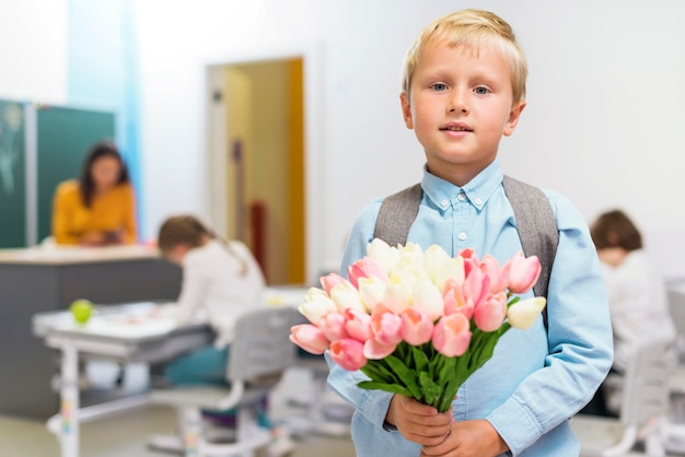 正面に彼の先生のための花の花束を保持している小さな男の子 無料の写真