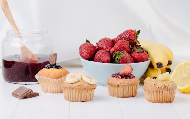 Front view muffins with bananas strawberries chocolate and lemon on a white surface Free Photo