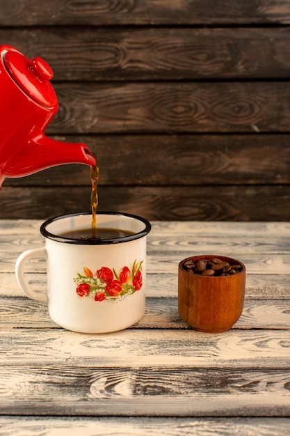 木製の机の上の赤いやかんから注ぐ熱いお茶の正面図 無料の写真