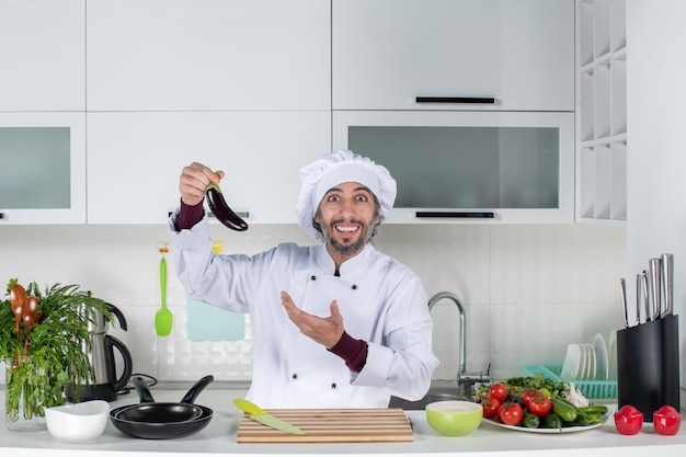 Free Photo Front View Satisfied Male Chef In Uniform Holding Aubergine In The Kitchen