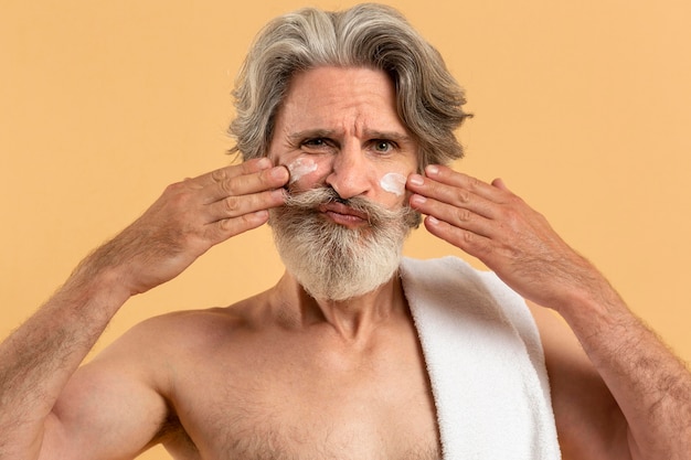  Front  view of senior man with beard  applying cream on face  