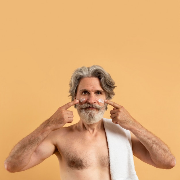  Front  view of smiley elder man with beard  applying cream 