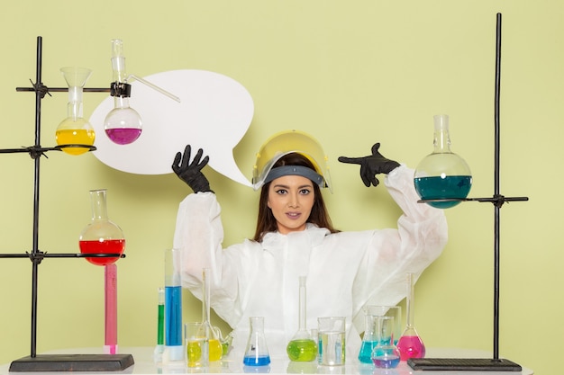 緑の壁の仕事化学実験室化学女性科学に白い看板を保持している特別な防護服の正面図若い女性化学者 無料の写真