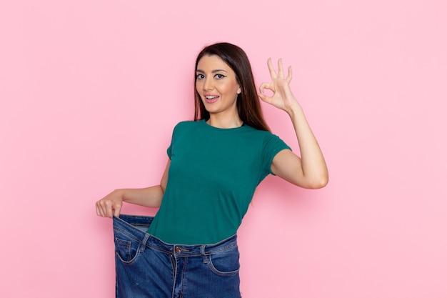 ピンクの壁に彼女のスリムな体を示す緑のtシャツの正面図若い女性ウエストスポーツエクササイズトレーニング美容スリムアスリート 無料の写真