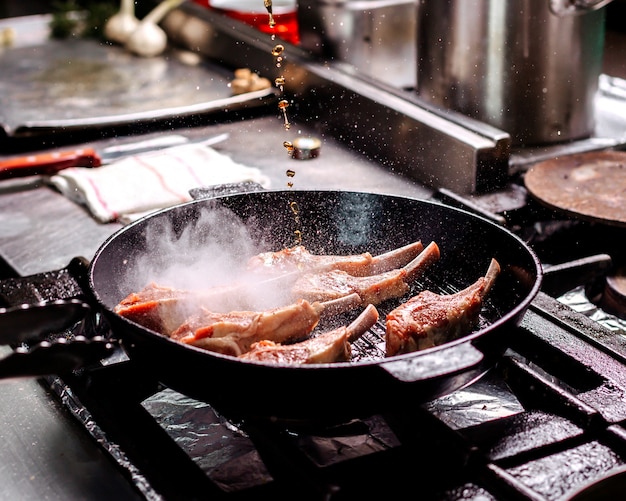 Frying ribs meat inside black pan in the kitchen Free Photo