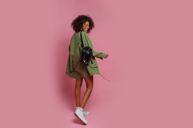 ピンクの背景のスタイリッシュな緑のジャケットに褐色肌の格好の良い女性の完全な長さの画像 ショッピングとファッションのコンセプトです 無料の写真