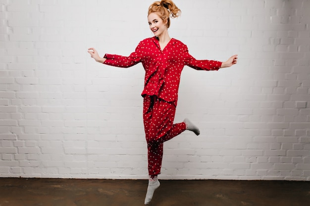 Free Photo Full Length Portrait Of Carefree Caucasian Girl Dancing In Red Pajamas On Light Wall Gorgeous Young Woman In Cute Sleepwear Jumping With Smile