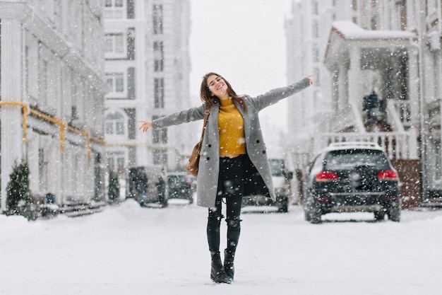 Full-length portrait of romantic european lady wears long coat in snowy day. outdoor photo of inspired brunette woman enjoying free time in winter city. Free Photo