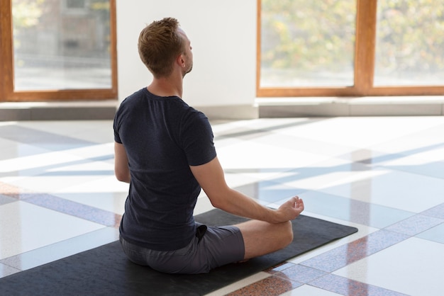 Free Photo | Full shot man doing sukhasana pose inside facing window