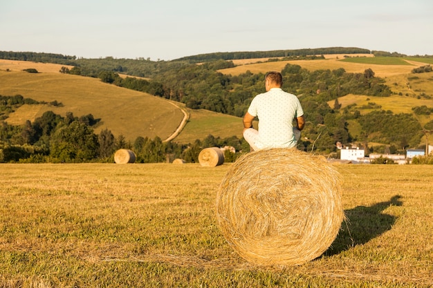 Full shot man sitting on roll of hays Free Photo