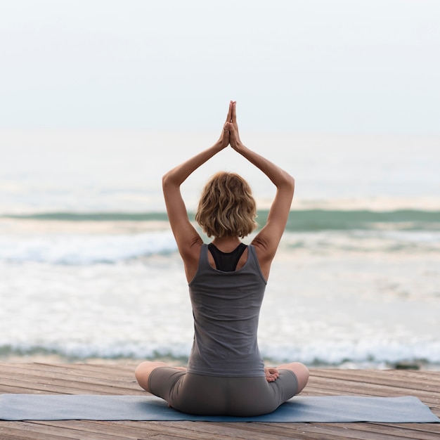 Free Photo | Full shot woman doing sukhasana pose outside facing sea