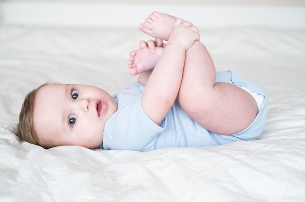 Premium Photo | Funny 6 months baby boy playing with legs, lying on bed ...