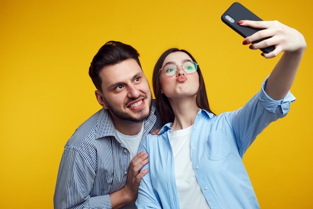 Premium Photo Funny Couple Makes Grimace Takes Selfie On Smartphone Over Yellow Wall