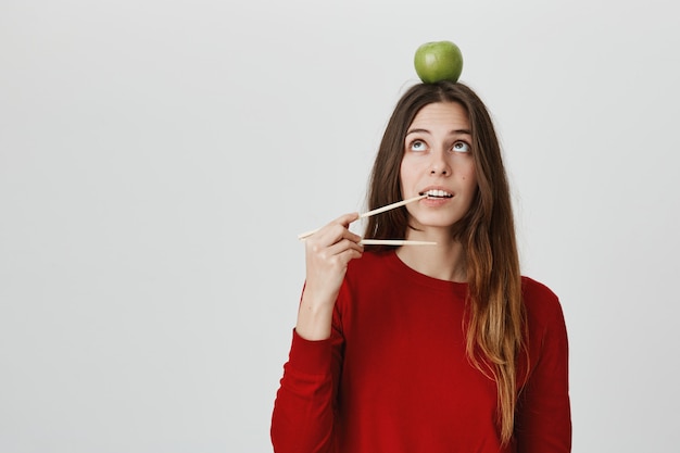 リンゴを食べて食べたい頭をかむ箸で面白いかわいい女の子 持ち帰りのコンセプト 無料の写真