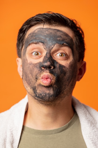 彼の顔に化粧マスクとオレンジ色のタオルを持つ面白い男 プレミアム写真