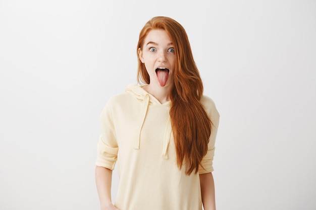Funny playful redhead girl showing tongue and looking excited Free Photo