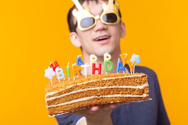 眼鏡をかけた面白いポジティブな男は お誕生日おめでとうの碑文と自家製ケーキを手に持っています プレミアム写真