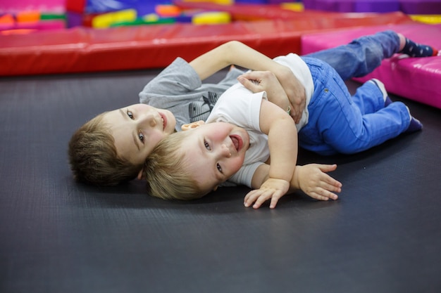 Premium Photo Funny Smiling Kids On Trampoline Older Brother Embraces The Younger Active Rest In The Children Center Boys Plays In Playing Room Little Friends Have Fun In Game Room Friendship